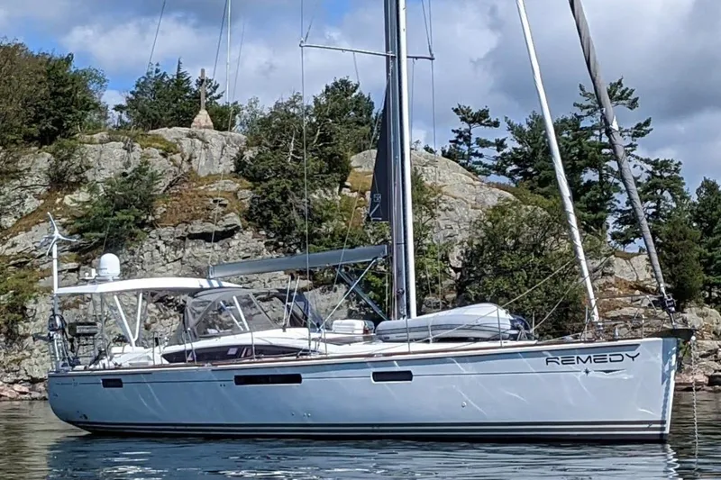 Remedy Yacht Photos Pics 2012 Jeanneau 57 sailboat named "Remedy" anchored near rocky shoreline.