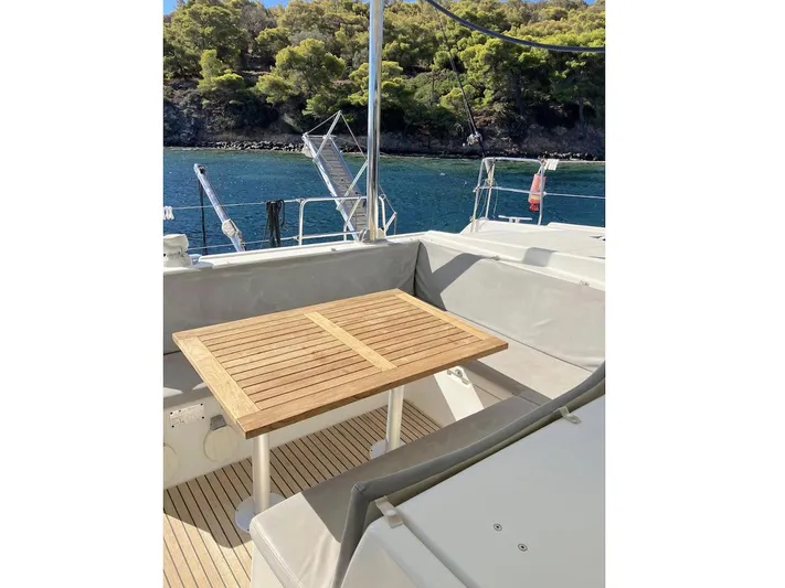 Kirlana Yacht Photos Pics Outdoor seating area on 2006 Lagoon 420 yacht with wooden table, overlooking serene water and lush greenery.