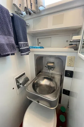 Huck Fin Yacht Photos Pics Compact bathroom in a 1966 Huckins Sportsman boat, featuring a stainless steel sink and modern amenities.