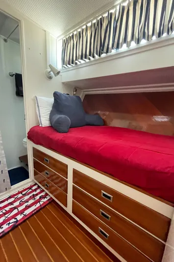 Huck Fin Yacht Photos Pics 1966 Huckins Sportsman cabin with red bedding, striped curtains, and wooden drawers.