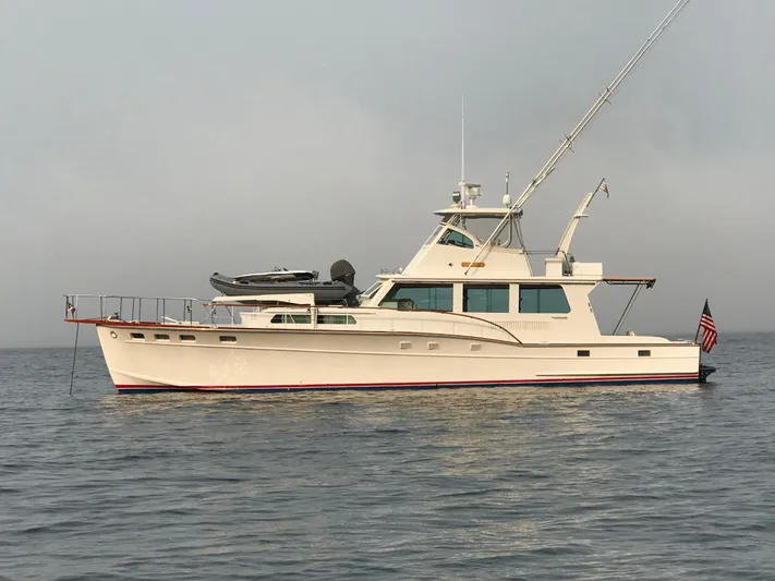 Huck Fin Yacht Photos Pics 1966 Huckins Sportsman yacht on calm water, featuring classic design and American flag.