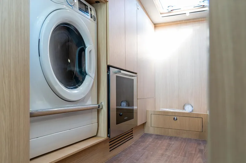 Superlux Yacht Photos Pics Laundry area inside 2023 Aquila 42 Yacht, featuring a washing machine and wooden cabinetry.
