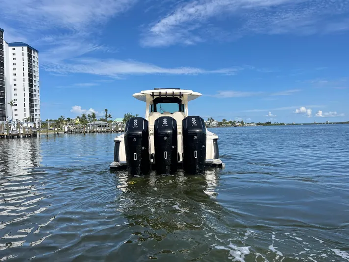  Yacht Photos Pics 2025 Scout 425 LXF boat with four engines on calm water, near a coastal cityscape.