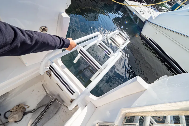  Yacht Photos Pics Person using ladder on 2018 Intrepid 475 Sport Yacht, docked by water.