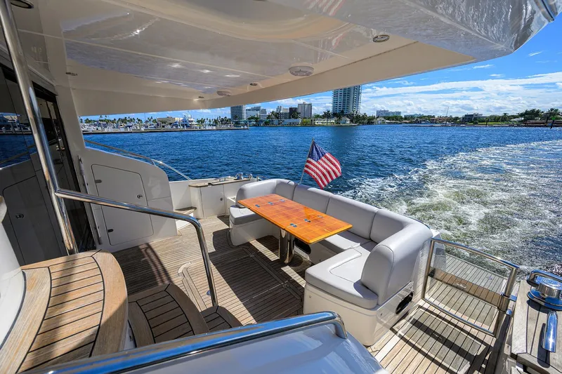 Tight Squeeze Yacht Photos Pics Luxurious 2016 Princess F64 yacht deck with seating, table, and American flag, cruising on a sunny day.
