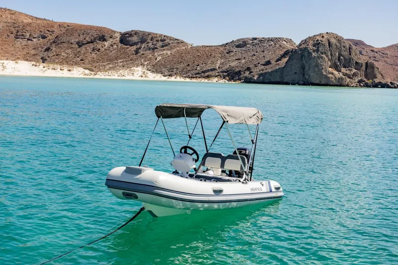 Mabinti Yacht Photos Pics Inflatable boat anchored in turquoise water near rocky coastline, clear sky above.