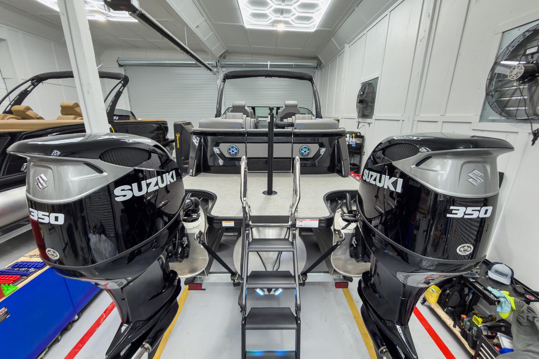2026 Godfrey Sanpan 27' Tritoon with twin Suzuki 350 engines in a garage setting.