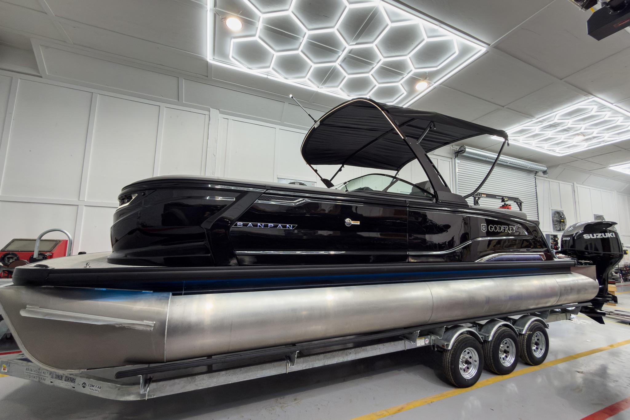 2026 Godfrey Sanpan 27' Tritoon boat in showroom, featuring sleek design and twin engines.