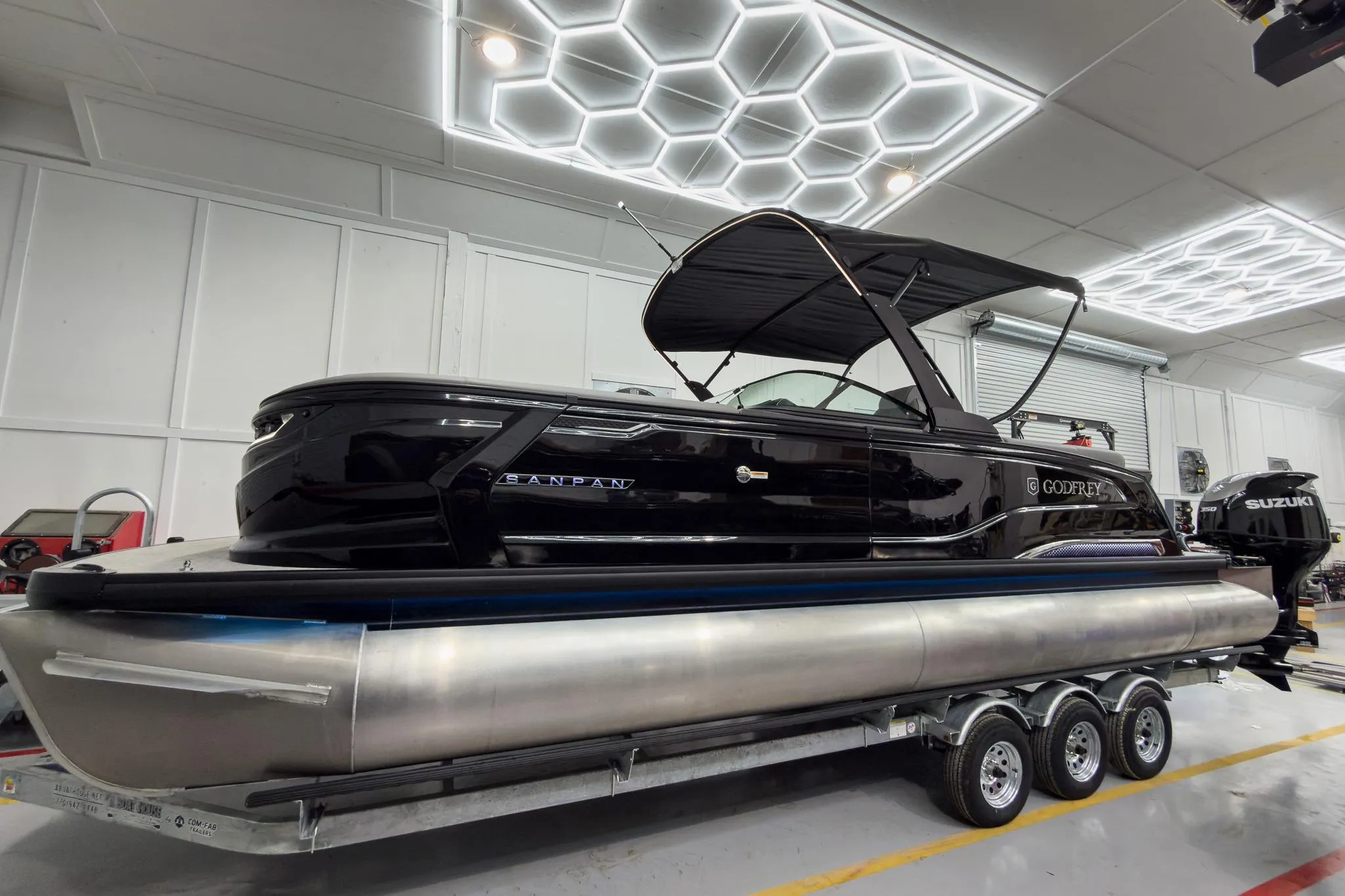 2026 Godfrey Sanpan 27' Tritoon boat in showroom, featuring sleek design and twin engines.
