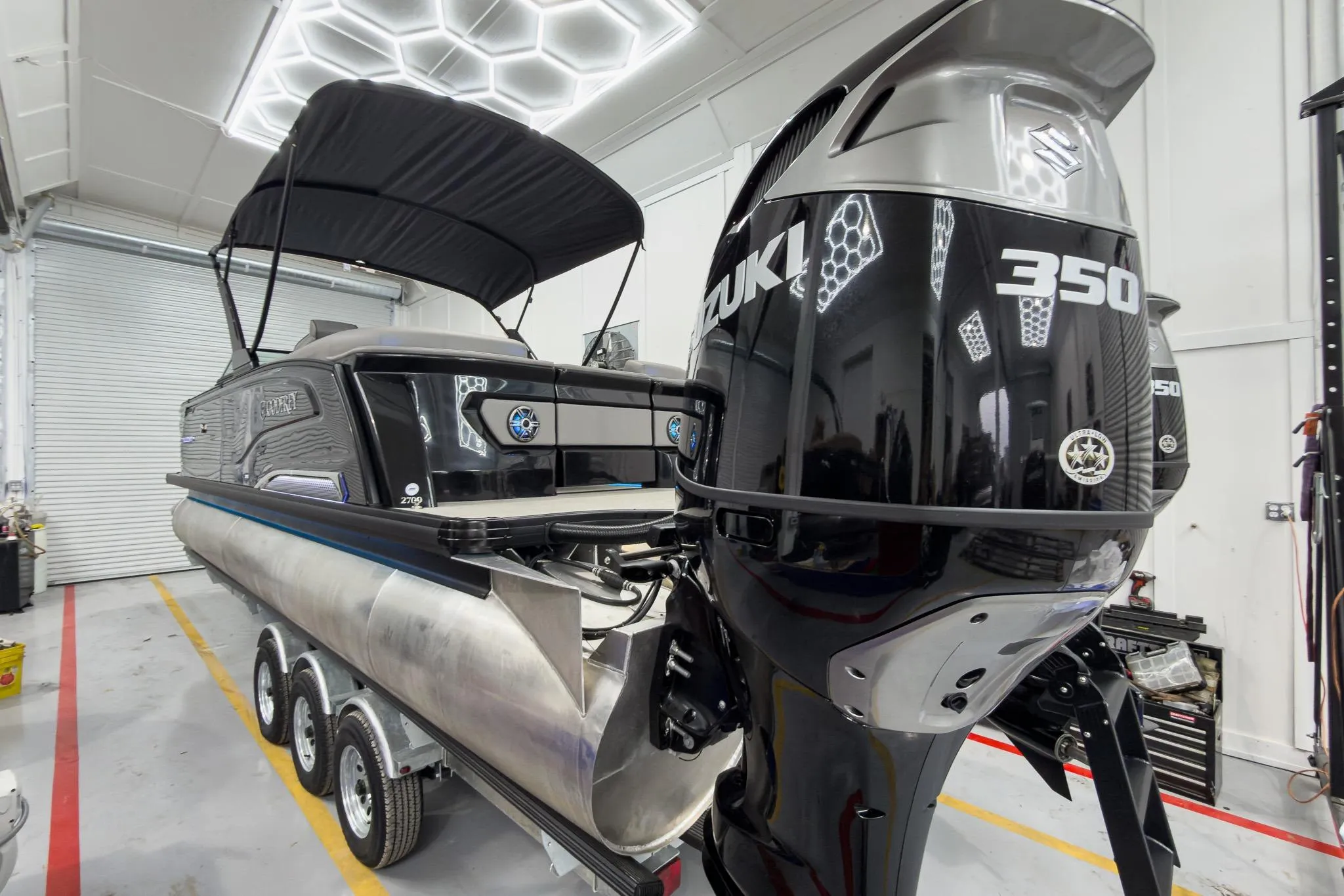 2026 Godfrey Sanpan 27' Tritoon with Suzuki 350 engine in a garage setting.