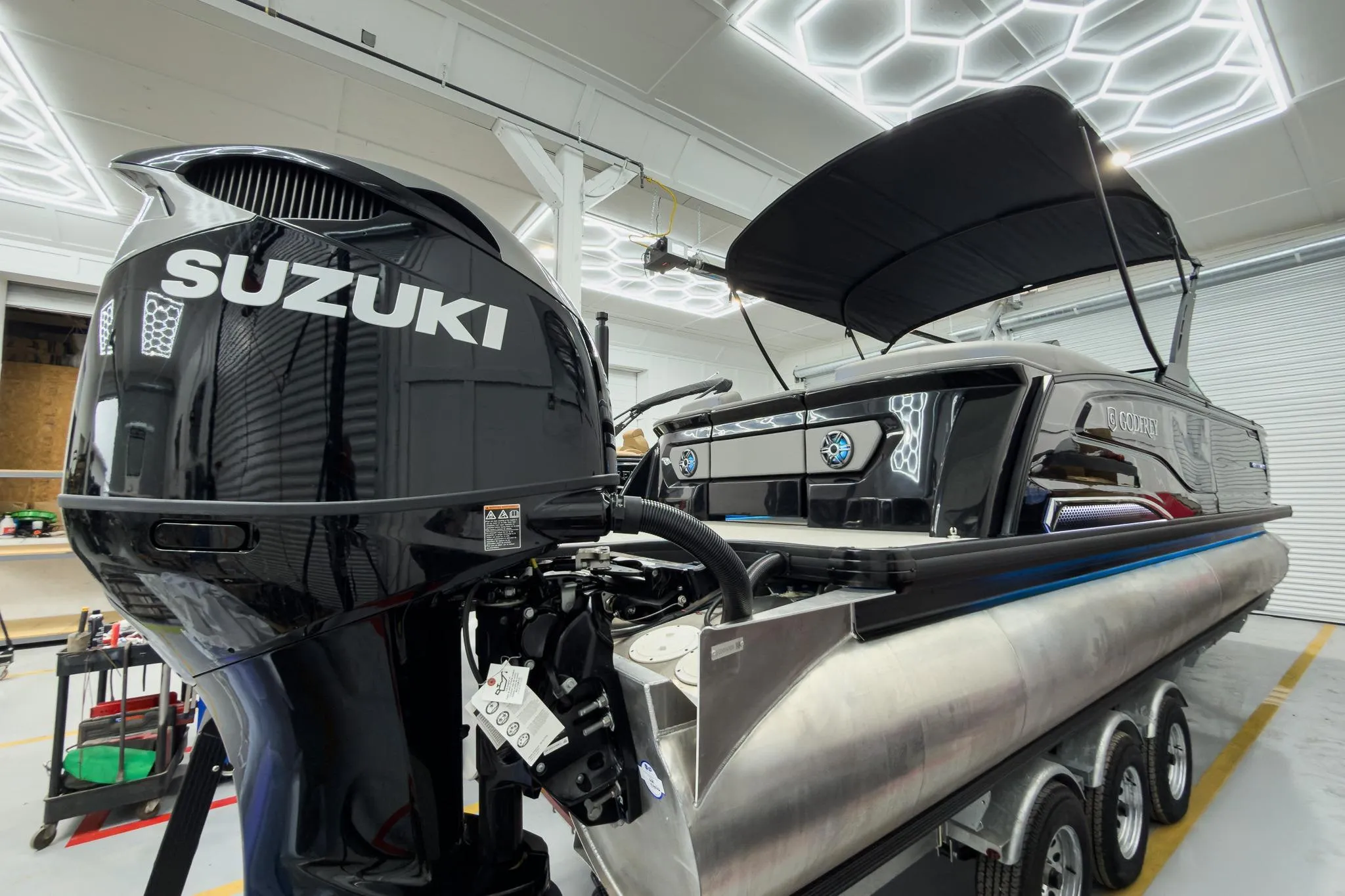 2026 Godfrey Sanpan 27' Tritoon with Suzuki engine in a modern showroom.