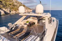 Luxurious 2007 Custom Line 97 yacht with sun loungers and dining area, anchored near scenic coastline.