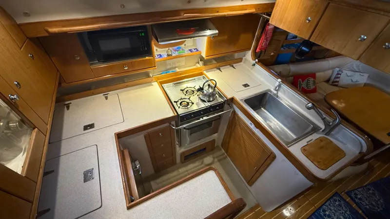  Yacht Photos Pics 2004 Catalina 470 yacht kitchen with stove, sink, microwave, and wooden cabinetry.