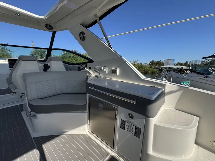  Yacht Photos Pics 2024 Sea Ray Sundancer 320 Outboard interior with seating and kitchenette under clear blue sky.