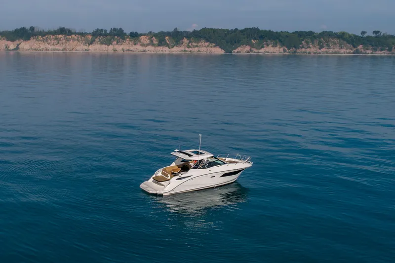At Times Yacht Photos Pics 2019 Sea Ray Sundancer 320 yacht cruising on calm blue waters near a scenic coastline.