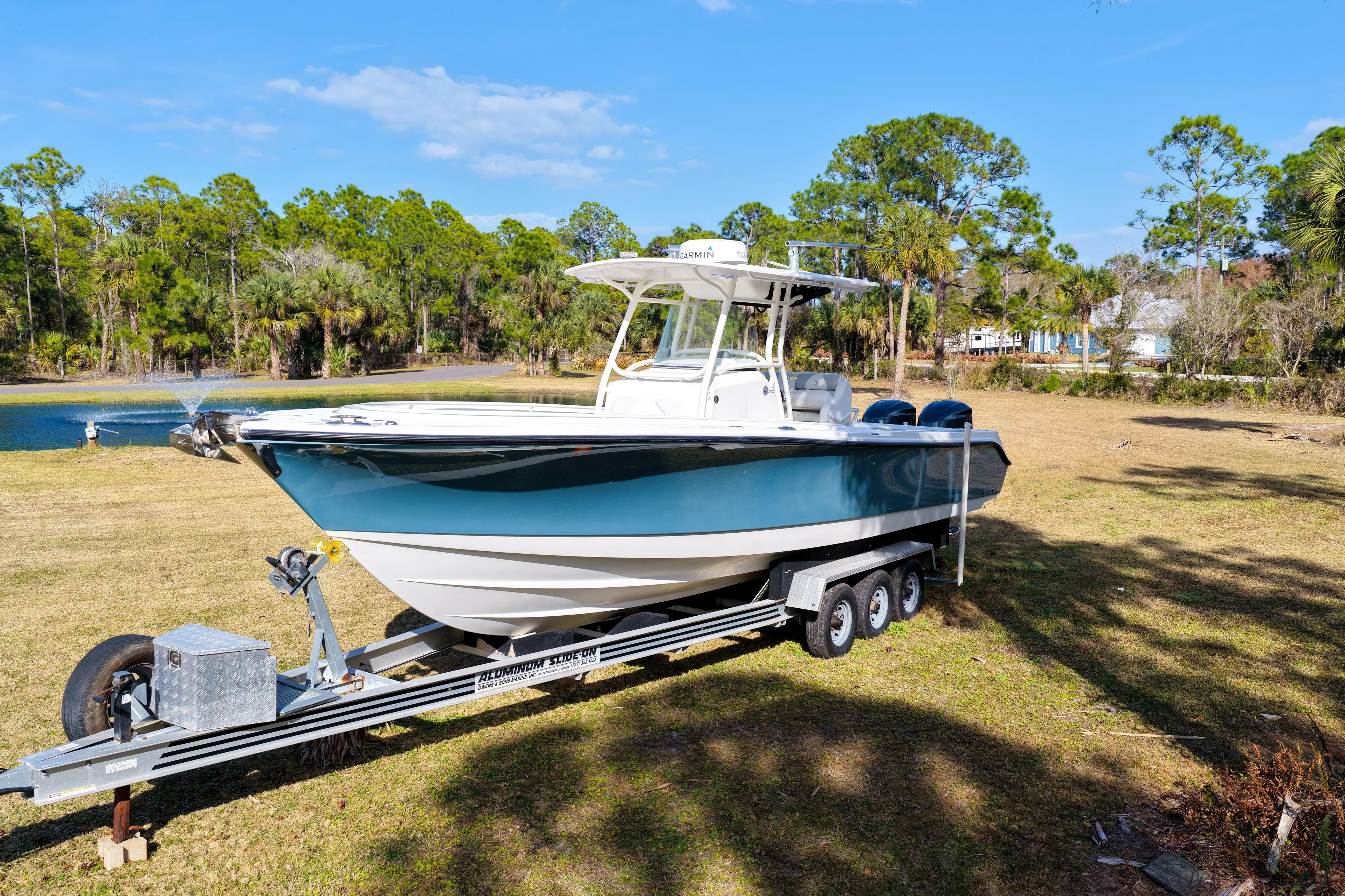  Yacht Photos Pics 2011 Edgewater 318CC boat on trailer, parked on grassy area near trees and pond.