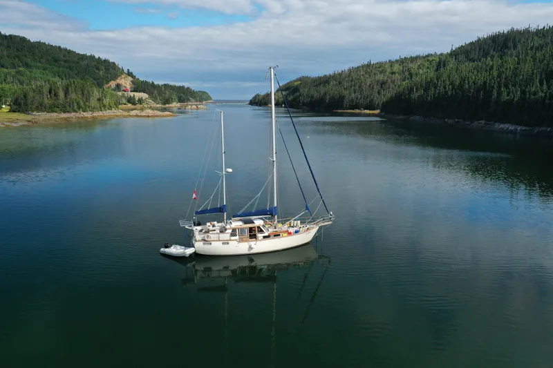 Latte Yacht Photos Pics Sailboat Nauticat 38 (1987) anchored in a serene, forested bay under a cloudy sky.