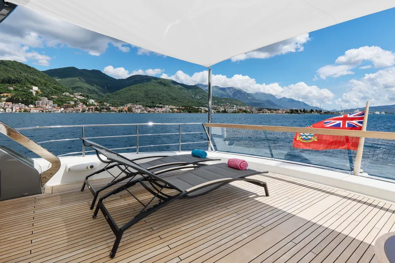  Yacht Photos Pics Luxurious Sanlorenzo SX88 yacht deck with sun loungers, scenic ocean view, and mountains in the background.