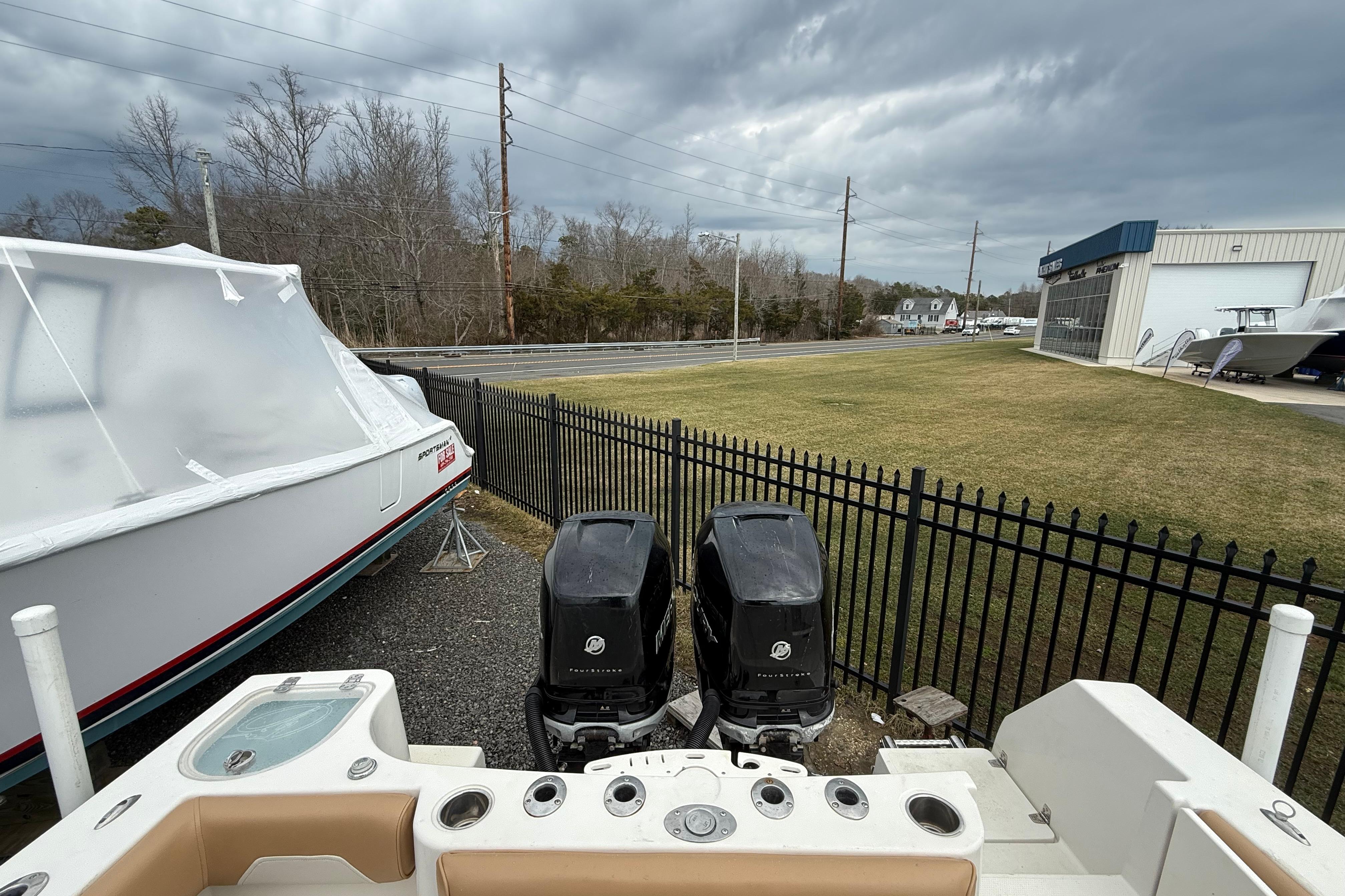 2015 Sailfish 2860 CC boat with dual outboard motors, parked near a fenced area.