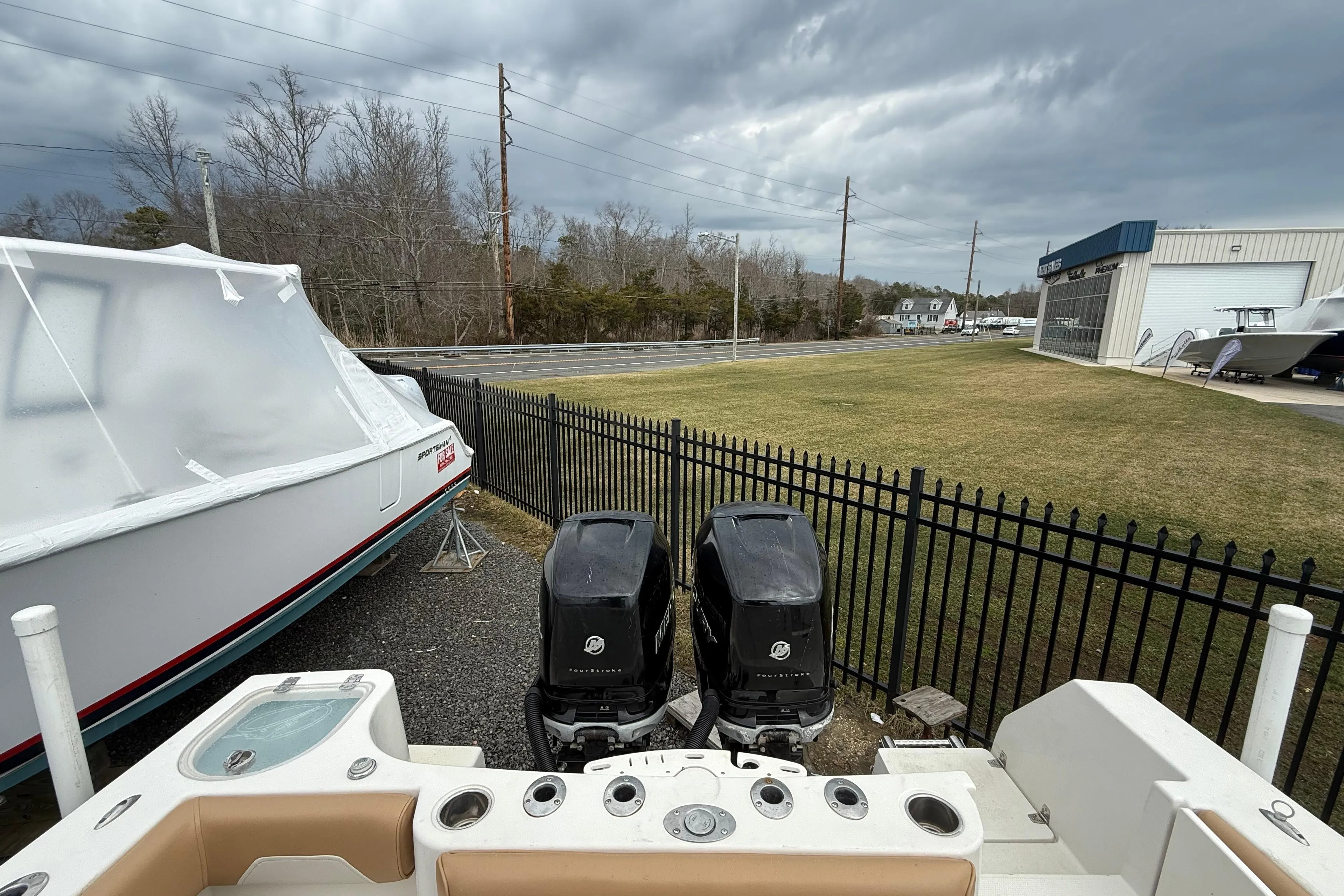 2015 Sailfish 2860 CC boat with dual outboard motors, parked near a fenced area.