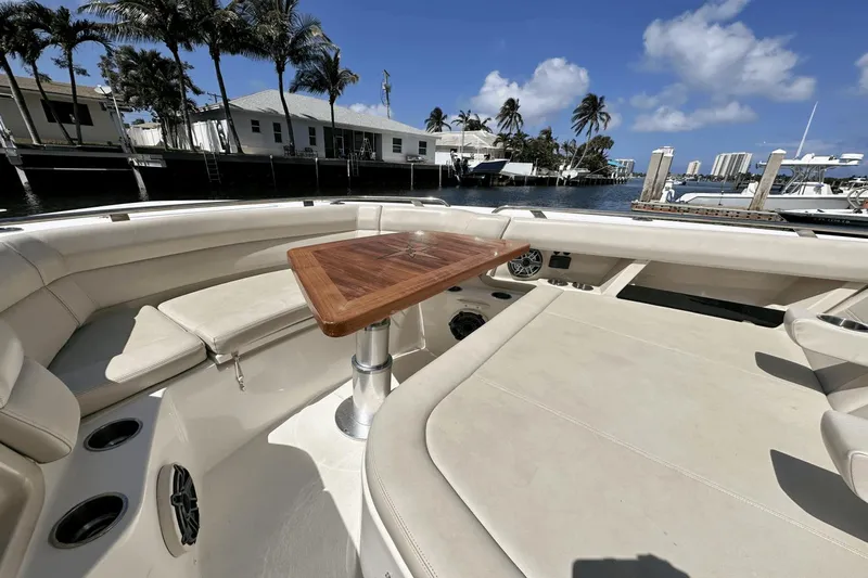  Yacht Photos Pics 2019 Boston Whaler 350 Realm boat interior with wooden table and seating, docked by palm trees.