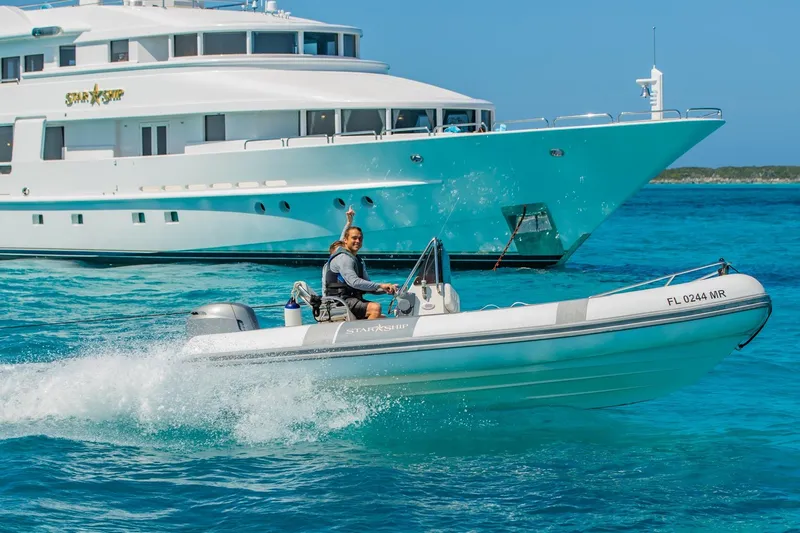 Starship Yacht Photos Pics Man driving a small boat near a large yacht, Van Mill Custom 1988, in clear blue waters.