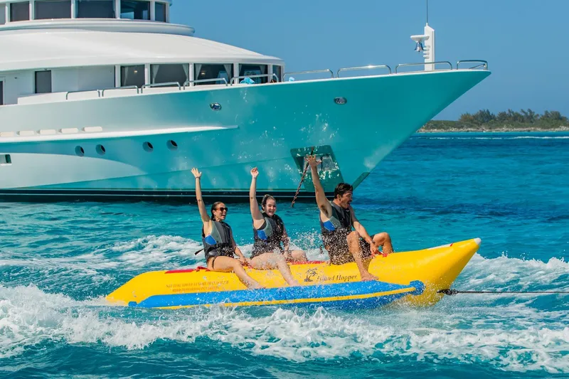 Starship Yacht Photos Pics People enjoying a banana boat ride near a Van Mill Custom yacht, 1988 model, in clear blue waters.