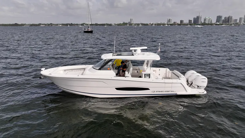  Yacht Photos Pics 2023 Regal 38 SAV boat cruising on open water with city skyline in background.