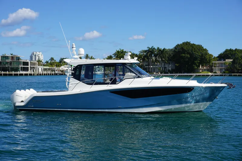 Rendezvous Yacht Photos Pics 2021 Boston Whaler 405 Conquest boat cruising on a sunny day, with waterfront buildings in the background.