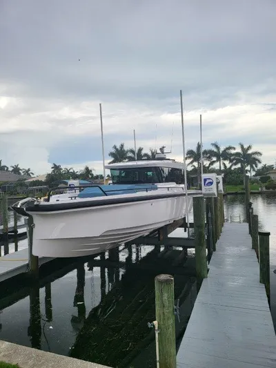  Yacht Photos Pics 2024 Axopar 37 XC CROSS CABIN docked by palm trees, overcast sky.