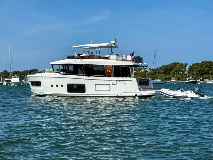 In Stock Yacht Photos Pics 2026 Beneteau Swift Trawler 54 cruising on a sunny day with a small boat in tow.