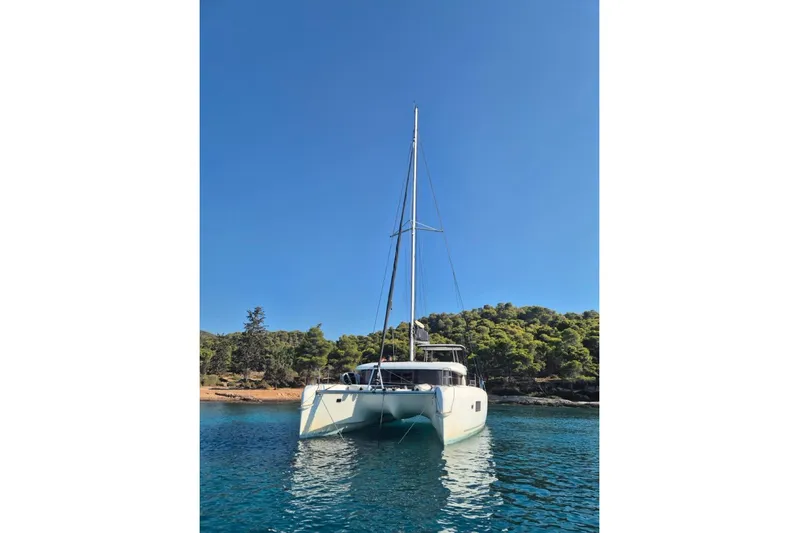  Yacht Photos Pics 2020 Lagoon 42 catamaran anchored in clear blue water near a forested shoreline.