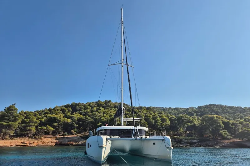  Yacht Photos Pics 2020 Lagoon 42 catamaran anchored in a serene, forested bay under a clear blue sky.
