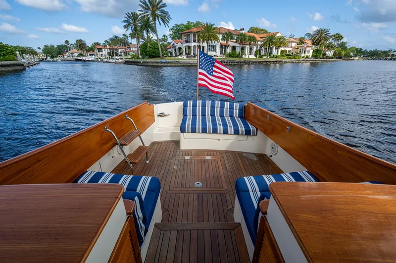 Miss Behave Yacht Photos Pics Hinckley Picnic Boat 37 MKIII, 2017, with striped seating, American flag, on a scenic waterfront.