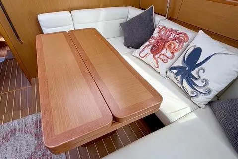 Rising Sun Yacht Photos Pics 2016 Jeanneau Sun Odyssey 50 DS interior with wooden table, white seating, and nautical-themed pillows.