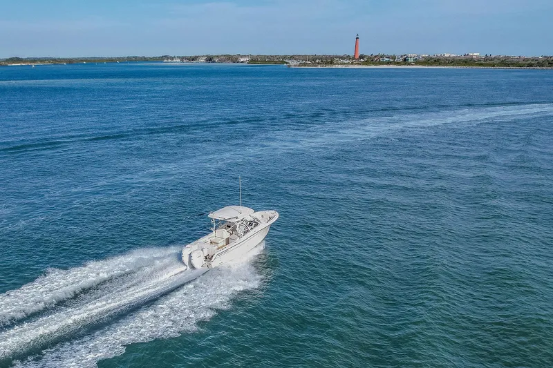 Fin & Tonic Yacht Photos Pics 2024 Grady-White Freedom 275 boat cruising on open water near a distant lighthouse.