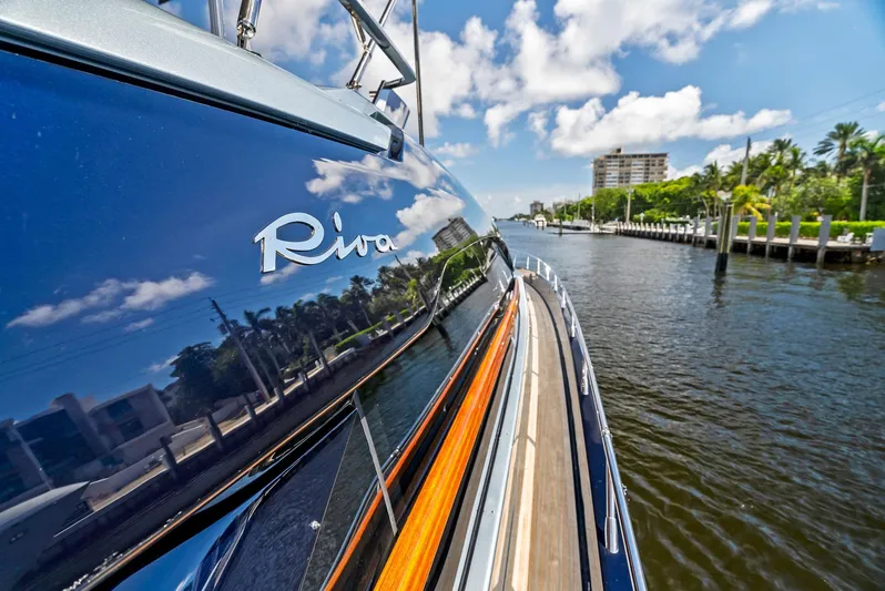 Knot Normal Yacht Photos Pics Riva 66' Ribelle 2020 yacht reflecting water and sky, docked near palm trees and buildings.