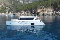2020 Catamaran Ocean Beast 65 sailing in clear waters near rocky coastline.