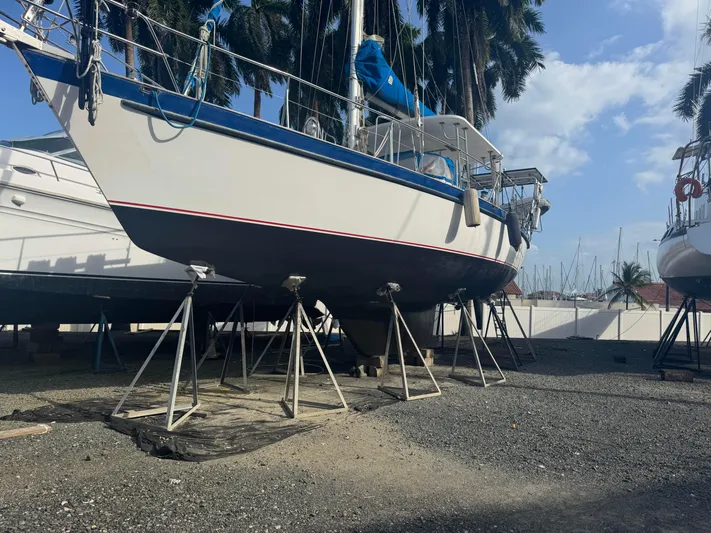 Sv Indago Yacht Photos Pics 1991 Tayana 47 CC sailboat on stands in a boatyard, surrounded by palm trees.