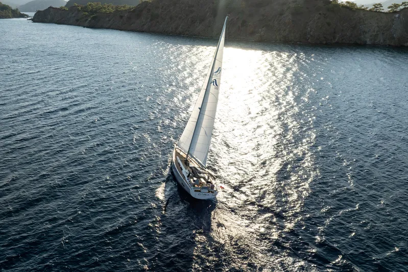 Hanse 588 Yacht Photos Pics Sailing yacht Hanse 588 (2024) gliding on sunlit waters near a rocky coastline.