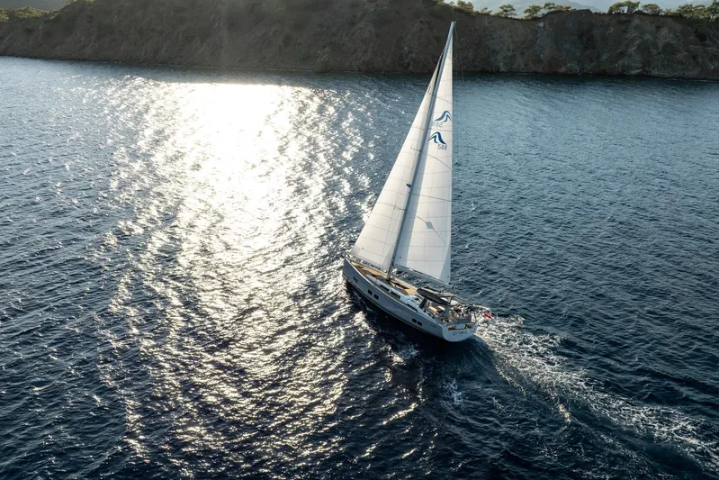 Hanse 588 Yacht Photos Pics Sailing yacht Hanse 588 (2024) gliding on sunlit ocean waters near a rocky coastline.