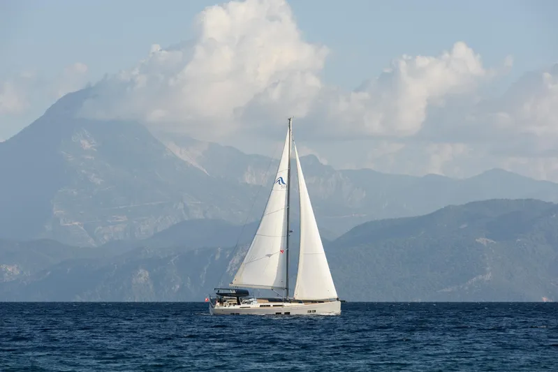 Hanse 588 Yacht Photos Pics 2024 Hanse 588 sailboat cruising on open sea with mountainous backdrop.