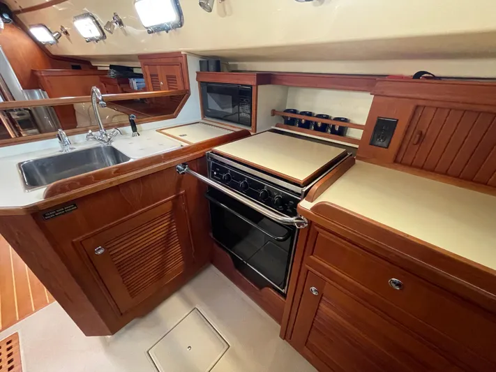  Yacht Photos Pics Galley kitchen in 2002 Island Packet 380 sailboat with stove, sink, and wooden cabinetry.