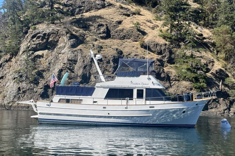 Positive Space Yacht Photos Pics 1987 DeFever Trawler boat anchored near rocky shoreline with trees.