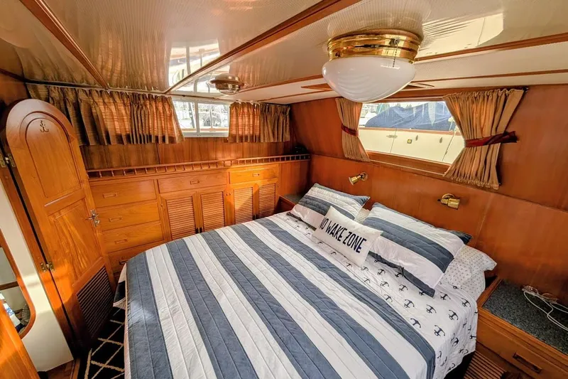Positive Space Yacht Photos Pics Luxurious 1987 DeFever Trawler bedroom with striped bedding and wooden cabinetry.
