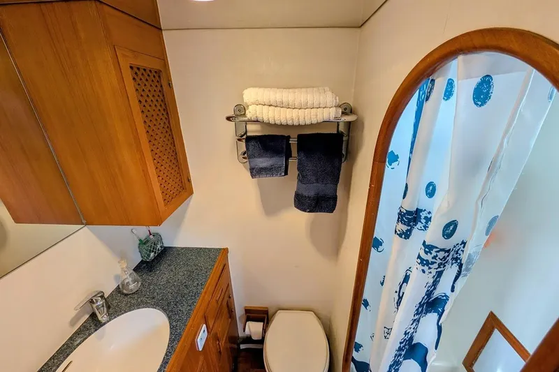 Positive Space Yacht Photos Pics 1987 DeFever Trawler bathroom with wooden cabinetry, sink, and nautical-themed shower curtain.