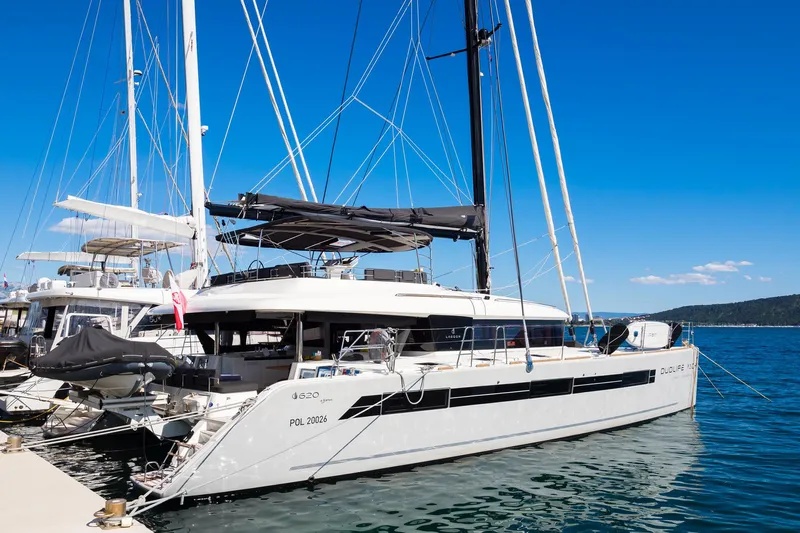 Duolife Yacht Photos Pics 2019 Lagoon 620 Essence catamaran docked at marina under clear blue sky.