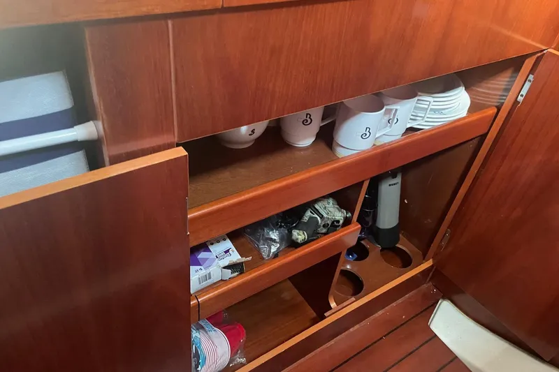 Gemini's Escape II Yacht Photos Pics Wooden cabinet interior on 2005 Beneteau Oceanis 42CC yacht, featuring mugs and storage shelves.