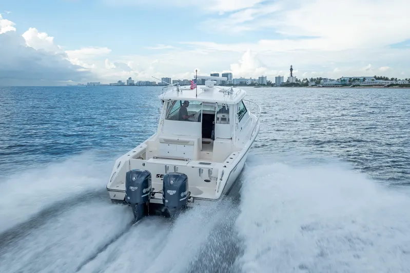 "seven C's" Yacht Photos Pics 2011 Pursuit OS 345 Offshore boat cruising on open water near city skyline.