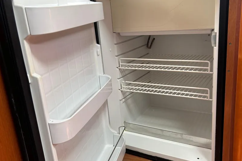  Yacht Photos Pics Empty refrigerator inside 2015 Beneteau Oceanis 48 yacht, featuring wire shelves and door storage.
